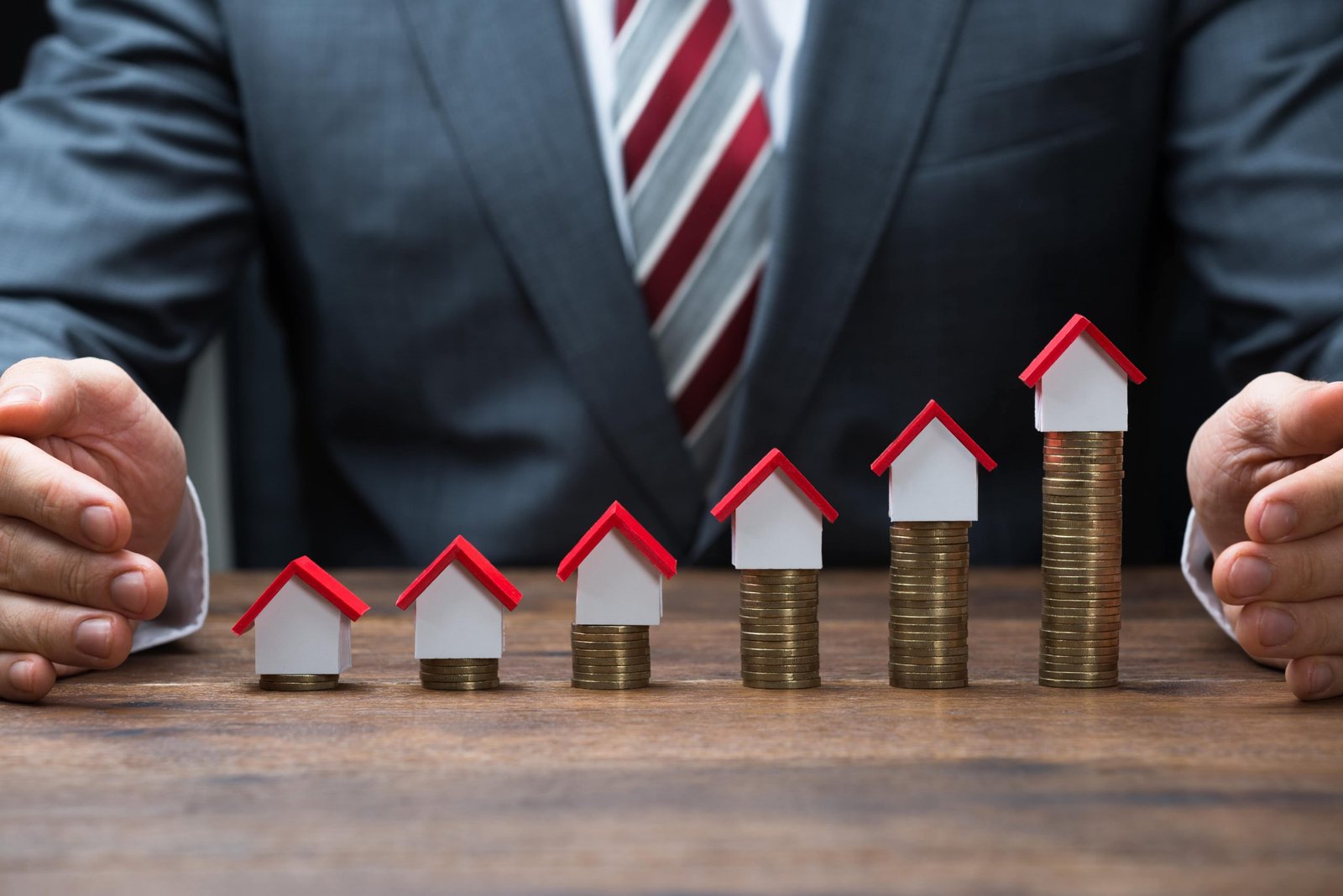 Midsection of businessman protecting house models on stacked coins at table