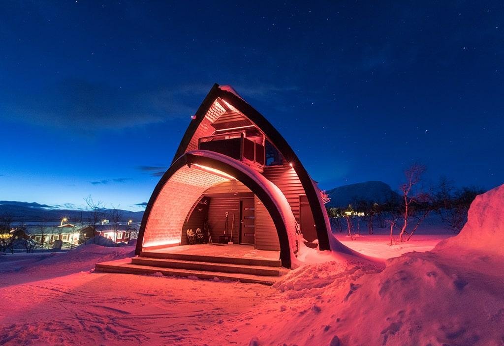 A two story cabin with pink LED lights lighting it up and a clear deep blue sky in the background