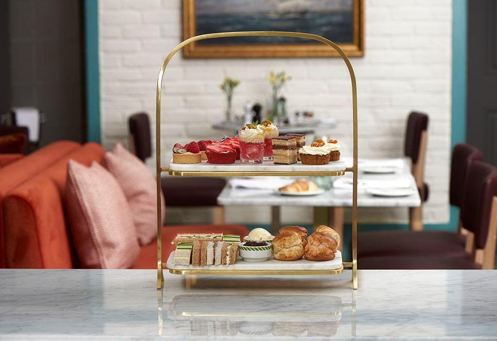 An afternoon tea spread with cakes, perfectly cut rectangle sandwiches and scones