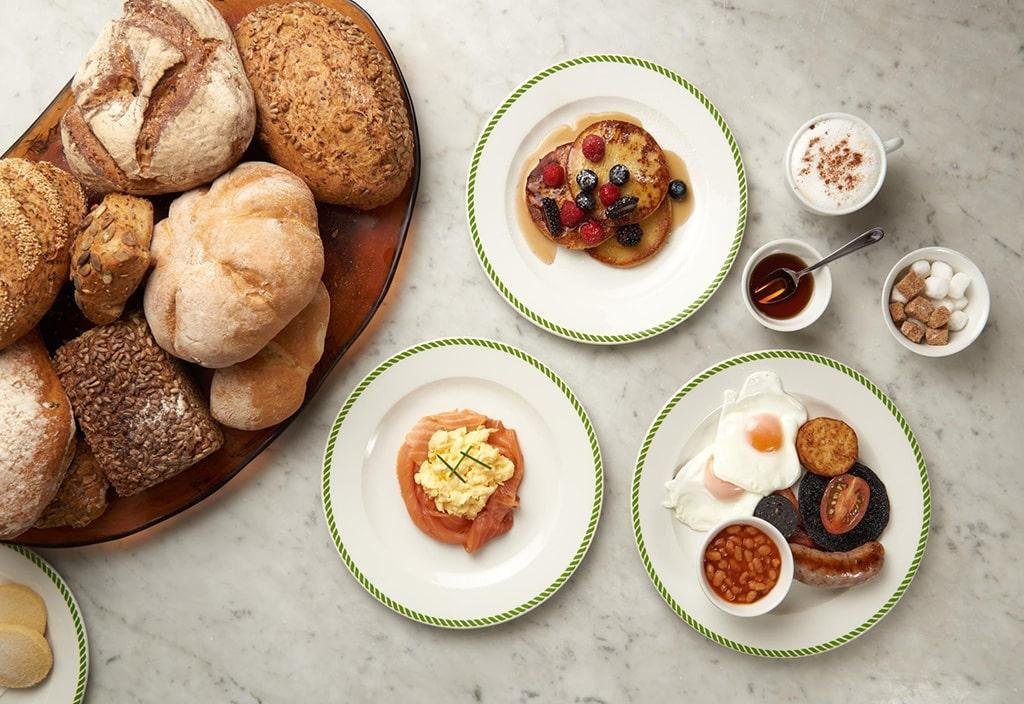 A platter of breakfast dishes including bread, salmon and eggs, pancakes and an english breakfast