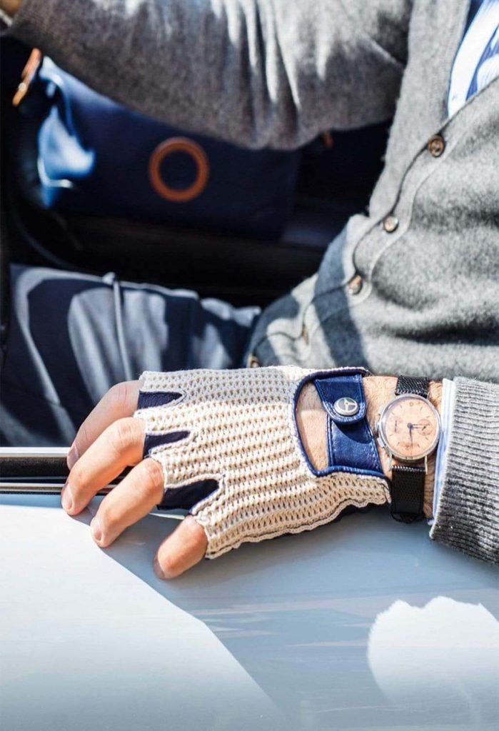 A close up of a man sitting in his car with fingerless beige and royal blue gloves and a watch