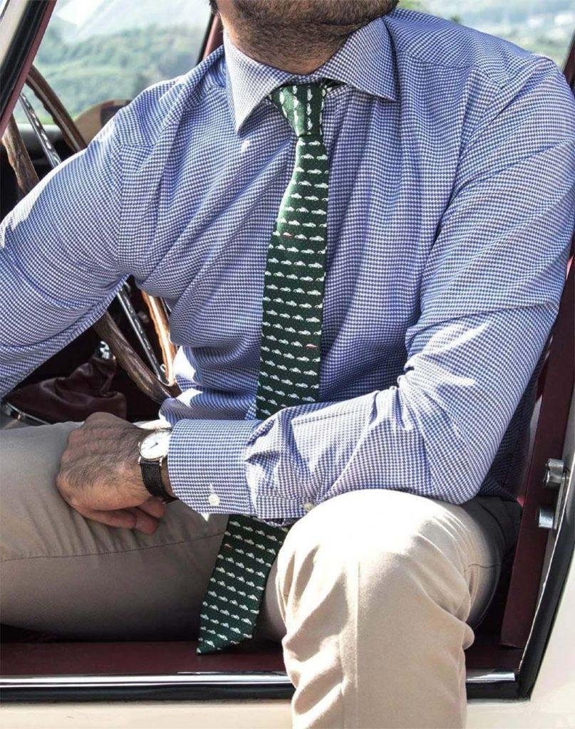 A close up of a mans torso wearing a light blue button up shirt and a green and white patterned tie