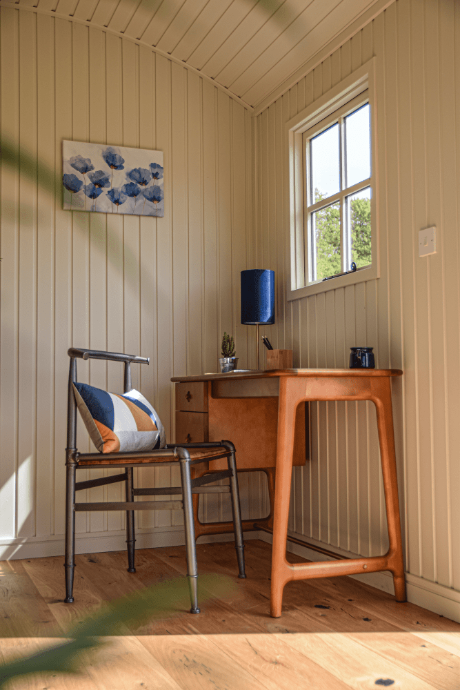 A well thought out and lit space, carefully designed with a smooth wood work table and metal chair exaggerated through the creme coloured walls, completed with a plush cushion dressed in gold, navy and white triangles.